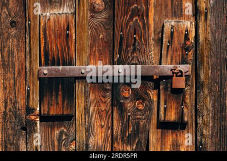 Un vecchio lucchetto corroso e arrugginito sulla porta del fienile di legno come sfondo Foto Stock