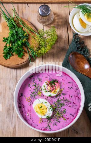 Tradizionale zuppa estiva fredda di barbabietole con cetrioli, uova e panna acida su fondo di legno. Stile rustico. Foto Stock