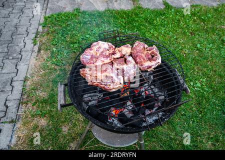 Vecchio grill nero all'aperto con bistecca di maiale marinata a fette in giardino. Foto Stock