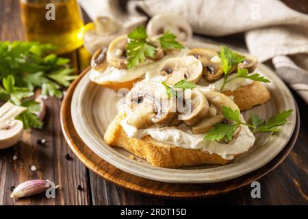 Panino tostato con baguette, pane con formaggio morbido e funghi grigliati su un tavolo rustico in legno. Bruschetta fatta in casa con funghi. Foto Stock