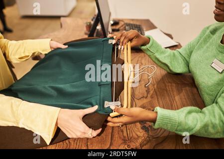 Primo piano di una donna che consegna capi di abbigliamento all'assistente al banco per l'acquisto in boutique Foto Stock