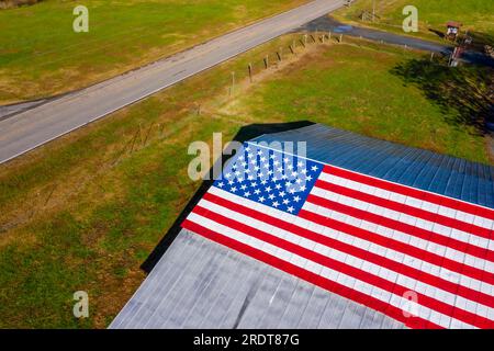 Una strada di campagna con una bandiera americana dipinta su un fienile vicino a una fattoria negli Stati Uniti Foto Stock