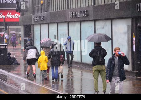 Manchester, Regno Unito, 23 luglio 2023. Gli acquirenti combattono attraverso la pioggia torrenziale a Market Street, nel centro di Manchester, nel Regno Unito, mentre il Met Office emette un avvertimento giallo per il Galles del Nord, Merseyside, Greater Manchester e Newcastle-upon-Tyne. È probabile che in alcune località si verifichino allagamenti. Credito: Terry Waller/Alamy Live News Foto Stock