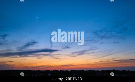 Luna a mezzaluna nel cielo incandescente del crepuscolo che svanisce nel blu con l'orizzonte scuro Foto Stock