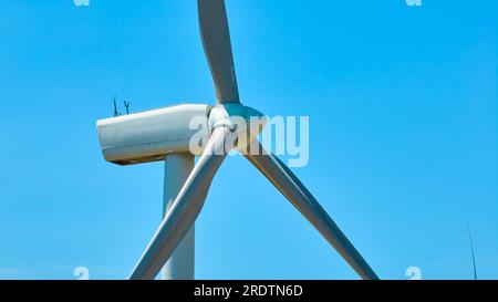Primo piano della turbina eolica e delle pale con un cielo azzurro dietro di essa un colpo di drone aereo Foto Stock