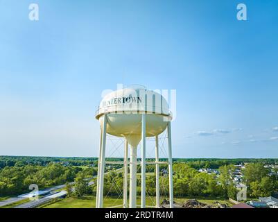 Torre aerea bianca dell'acqua di Huntertown con alberi verdi distanti e cielo blu Foto Stock