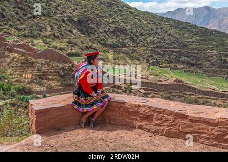 Donna indigena quechua peruviana sulle mura inca in abbigliamento tradizionale, Tipon, Cusco, Perù. Foto Stock