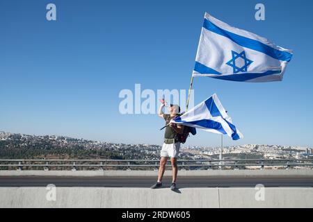 Israele. 22 luglio 2023. Un protestore contro la riforma beve acqua mentre tiene la bandiera israeliana sulla strada d'ingresso a Gerusalemme. Decine di migliaia di manifestanti contro la riforma sventolano la bandiera israeliana mentre si arrampicano sulla strada d'ingresso a Gerusalemme, terminando una marcia di 4 giorni a partire da Tel Aviv in una manifestazione contro la legislazione in corso di revisione legale. Gerusalemme, Israele. 22 luglio 2023. (Matan Golan/Sipa USA). Credito: SIPA USA/Alamy Live News Foto Stock