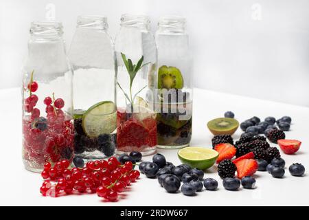 Ribes rosso, fragole, mirtilli e more sul tavolo. Acqua frizzante in bottiglie di vetro. Copia spazio. Sfondo bianco Foto Stock