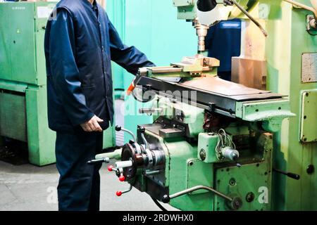 Un lavoratore maschio lavora su un più grande fabbro di ferro tornio, attrezzature per riparazioni, lavori di metallo in un'officina in un impianto metallurgico in un produ di riparazione Foto Stock