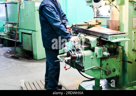 Un lavoratore maschio lavora su un più grande fabbro di ferro tornio, attrezzature per riparazioni, lavori di metallo in un'officina in un impianto metallurgico in un produ di riparazione Foto Stock