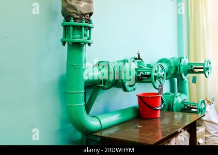 Perdita dalla valvola difettosa, montaggio sulla tubazione con una benna sotto di essa nello stabilimento di fabbrica. Concetto: Riparazione di tubi e valvole con gli attrezzi disponibili. Foto Stock