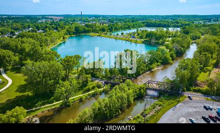 Scintillante laghetto blu turchese con lussureggianti alberi estivi e ponte ferroviario sul fiume che conduce al parco Foto Stock