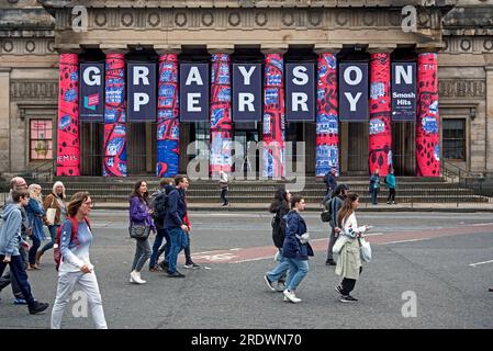Pedoni su Princes Street Walk vicino alla Royal Scottish Academy che pubblicizza la mostra di Grayson Perry, parte del Festival di Edimburgo del 2023. Foto Stock