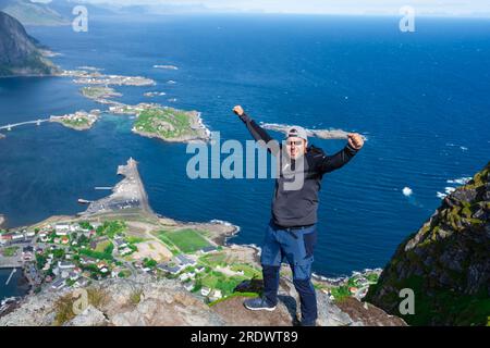 Rilassato e felice escursionista gode di una vista mozzafiato sulle cime di Reinebringen delle isole Lofoten, dei fiordi e della Norvegia Foto Stock