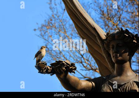 La statua dell'angelo si trova con il braccio esteso che tiene un ramo della pace. Appollaiato sul ramo è un solo uccello che prende in giro. Il concetto potrebbe includere fiducia, benevolo Foto Stock