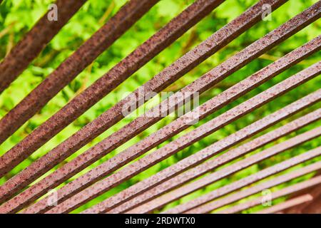 Luce solare brillante che riflette le barre di metallo arrugginite rosse con sfondo verde sfocato Foto Stock