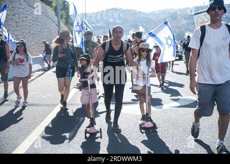 Gerusalemme, Israele. 22 luglio 2023. Un protestore contro la riforma spinge le sue figlie a scooters mentre scalano la strada d'ingresso a Gerusalemme durante la manifestazione. Decine di migliaia di manifestanti contro la riforma sventolano la bandiera israeliana mentre si arrampicano sulla strada d'ingresso a Gerusalemme, terminando una marcia di 4 giorni a partire da Tel Aviv in una manifestazione contro la legislazione in corso di revisione legale. (Immagine di credito: © Matan Golan/SOPA Images via ZUMA Press Wire) SOLO USO EDITORIALE! Non per USO commerciale! Foto Stock