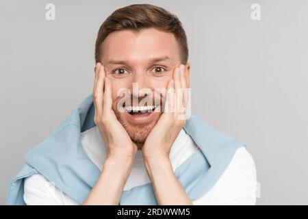 Bel sorridente uomo con la bocca aperta. Un ragazzo eccitato che si stupisce delle notizie positive. Faccia da primo piano. Foto Stock