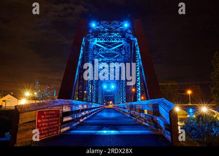 Direttamente sulla foto del ponte pedonale in legno attraverso le luci al neon blu sul vecchio ponte del treno a traliccio Foto Stock