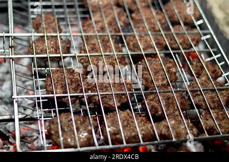 Polpette alla griglia kofta kufta di carne macinata di manzo in una rete a rete grigliata con manico su un carbone con fuoco e fuoco alla griglia, barbecue succoso Foto Stock