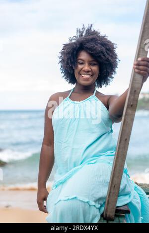 Ritratto di una bella donna con capelli neri seduti su una barca che guarda la fotocamera con un vestito azzurro. Cielo e nuvole sullo sfondo. Foto Stock