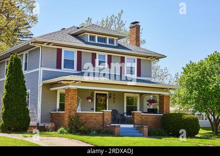 Davanti alla casa a due piani, giardino estivo, patio con veranda in mattoni, casa grigia, persiane rosse Foto Stock