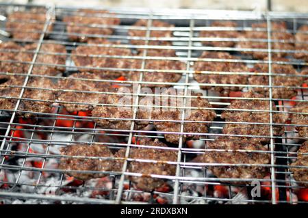 Polpette alla griglia kofta kufta di carne macinata di manzo in una rete a rete grigliata con manico su un carbone con fuoco e fuoco alla griglia, barbecue succoso Foto Stock