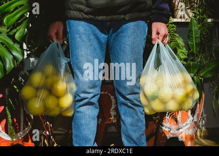 Uomo che torna dal mercato con due sacchetti pieni di limoni gialli freschi Foto Stock