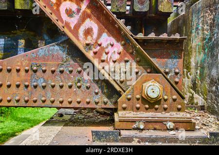 Rivetti in metallo arrugginito sulla vista laterale del ponte ferroviario e graffiti rosa con metallo blu corrosivo Foto Stock