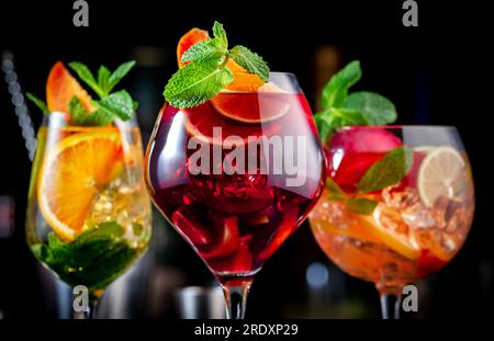 Cocktail alcolici estivi con sangria rosa, rosso, bianco, bevande con vino spagnolo, frutta, agrumi e ghiaccio. Sfondo nero del bancone del bar, utensili da bar in acciaio e. Foto Stock