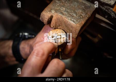 Le mani dei gioiellieri inseriscono un diamante in un anello con un burin. Goldsmith lavora per creare un gioiello d'oro nella sua bottega di gioielli. Foto Stock