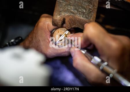 Le mani dei gioiellieri inseriscono un diamante in un anello con un burin. Goldsmith lavora per creare un gioiello d'oro nella sua bottega di gioielli. Foto Stock