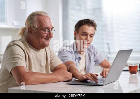 Giovane che mostra al nonno anziano come utilizzare varie applicazioni su un computer portatile Foto Stock