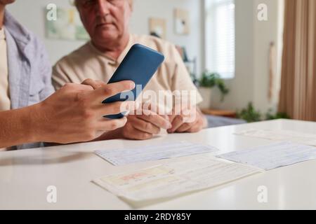 Immagine ravvicinata di un giovane che mostra al nonno come pagare le bollette online tramite app mobile Foto Stock