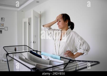Donna con la mano sulla testa in piedi vicino a un cestello per asciugare Foto Stock