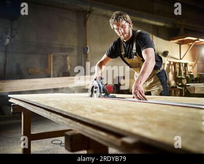 Pannelli per trefoli orientati al taglio di carpentiere con sega circolare in officina Foto Stock