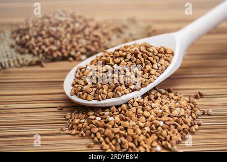 Un cucchiaio di legno ripieno di grano saraceno su un tappetino di bambù Foto Stock