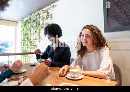 Giovane donna felice che passa del tempo con gli amici al bar Foto Stock