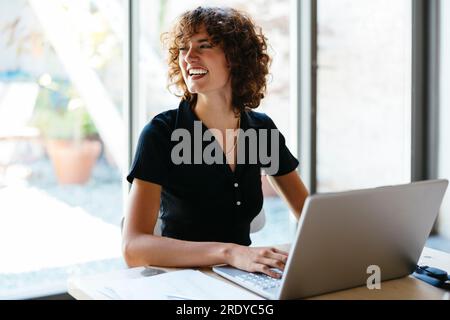 Felice giovane donna d'affari seduta con un computer portatile alla scrivania Foto Stock