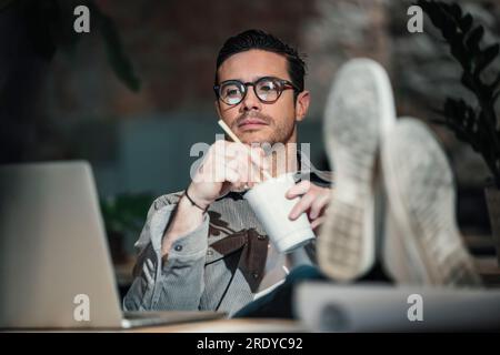 Figlio architetto che guarda un computer portatile e mangia noodles cinesi in ufficio Foto Stock