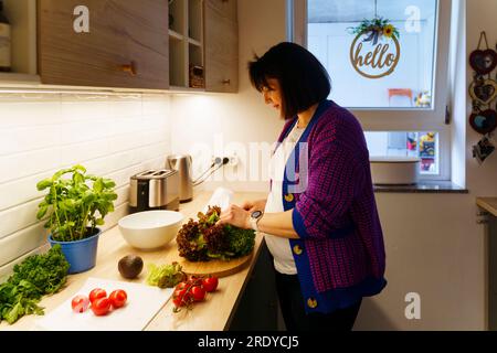Donna incinta con verdure che prepara cibo a casa Foto Stock
