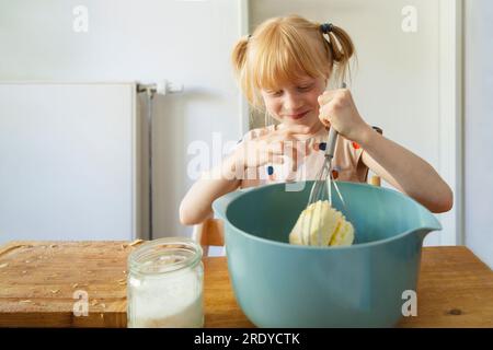 Ragazza sorridente che prepara l'impasto per torte con la frusta a casa Foto Stock