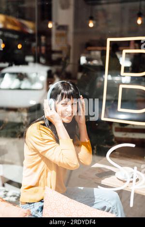 Donna sorridente che indossa cuffie wireless per ascoltare musica Foto Stock