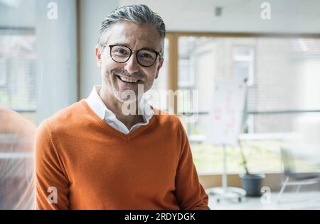 Uomo d'affari maturo sorridente che indossa occhiali in ufficio Foto Stock