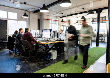 Uomini d'affari che camminano con i colleghi che lavorano alla scrivania in ufficio Foto Stock