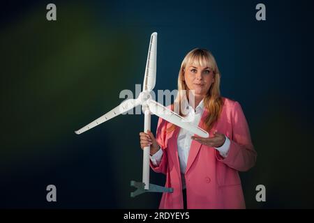 Donna d'affari in piedi con un modello di turbina eolica su sfondo blu Foto Stock