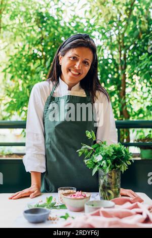 Chef sorridente che indossa grembiule vicino al tavolo nel balcone Foto Stock