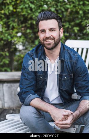 Uomo felice seduto sulla sedia di fronte alle piante Foto Stock