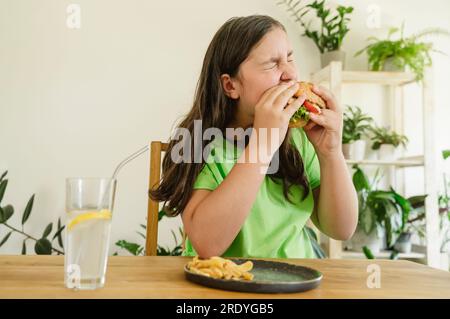 Ragazza che mangia hamburger con patatine fritte e soda a casa Foto Stock